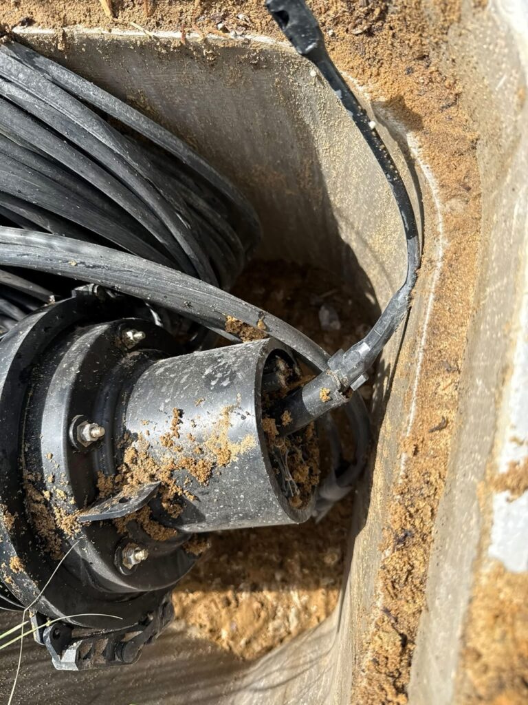 Splice closure in a vault with its end port open and packed with sand instead of sealed, coiled cable stored around it.