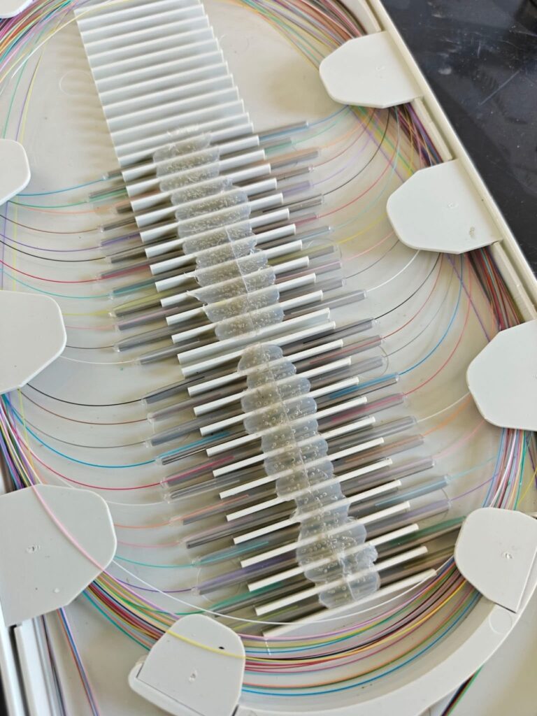 Splice tray with rows of fusion splice sleeves, many bubbled and cloudy from a bad heat shrink, color-coded fibers looped around the tray edges.
