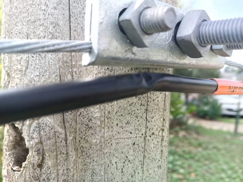 Fiber cable kinked and crushed just below a strand clamp on a wood pole.
