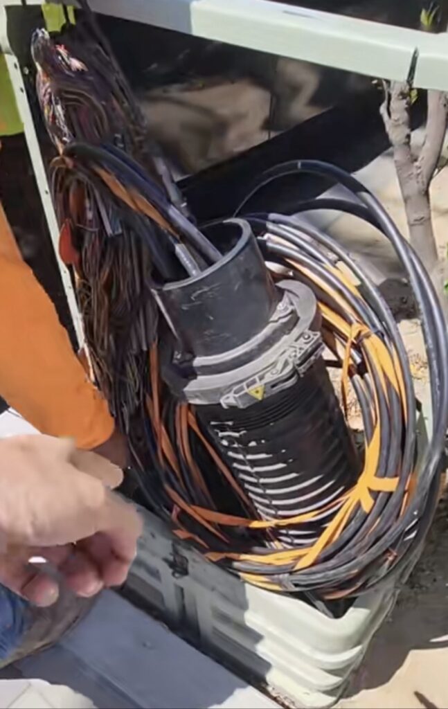 Dome splice closure left open with slack cable coiled in loops around the closure body inside a pedestal.